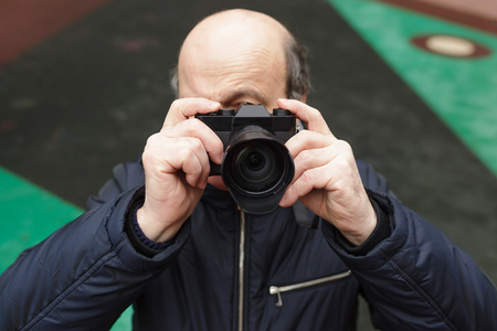 An elderly man with a mirrorless camera chooses a frame on the streetの写真素材