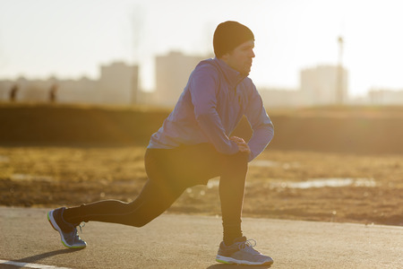 young man warms the muscles of his legs before jogging. Bright morning sun shinesの写真素材