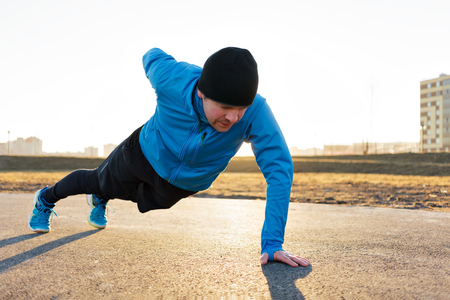 A young man in sportswear doing push-ups from the ground while training in the fresh airの写真素材
