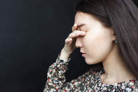 Asian girl closes her eyes with her palm. Headache or migraine, suffer from depression and loneliness.の写真素材