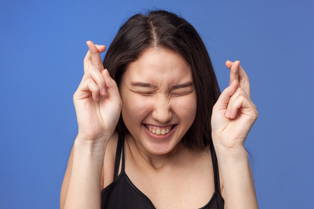 Asian girl crosses her fingers for good luck and closes her eyes. The anticipation of winning or luck.の写真素材