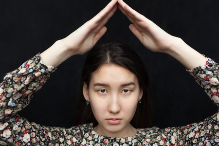Asian beautiful girl sad holds her hands like house roof and looks into the cameraの写真素材