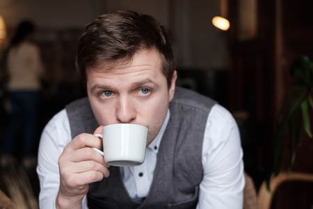 A young man in a white shirt and waistcoat breakfasts a cup of tea and thinks about the plans for the dayの写真素材