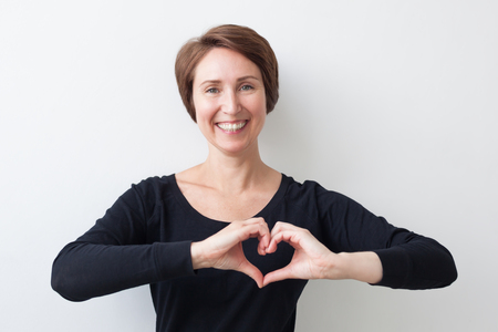 A beautiful middle-aged woman in a black T-shirt holds her hands in the chest in the form of a heart. Take care of your health.の写真素材