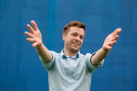 Success positive emotions. Happy young man in blue shirt stretchs hands ahead, wanting to hug someoneの写真素材