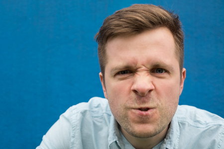 Face of an angry and furious caucasian man on a blue background.の写真素材