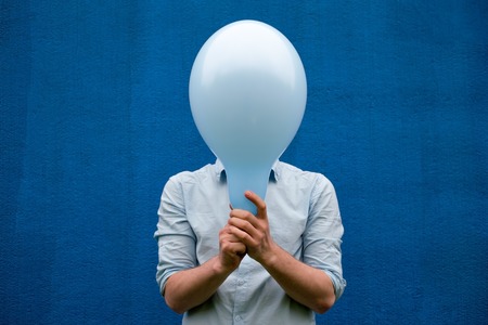 A white man covers his face with a blue balloon.の写真素材
