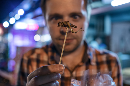 Caucasian young male eating cricket at night market in Thailand.の写真素材