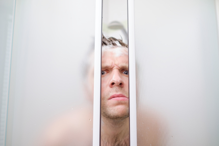 A young caucasian man peeks out of shower in soap.の写真素材