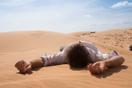 Man lie alone in the sunny desert. He is lost and out of breath. No water and energy.の写真素材