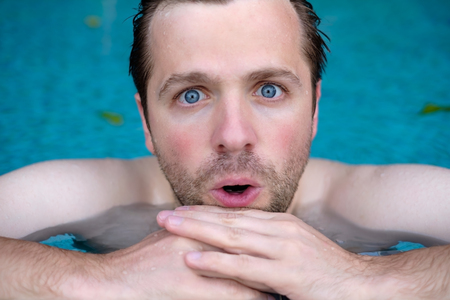 Man is shocked with news. He is closing his mouth. He is swimming in pool during vacation