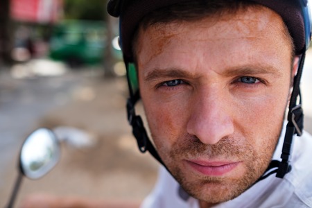 Young man in a helmet stays on a road of Asia watching at the camera. He is wearing helmet.の写真素材