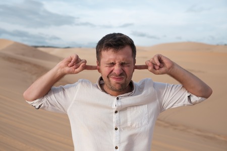 A middle-aged man stands alone in desert and closes his ears with his hands.の写真素材