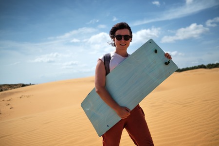 Caucasian girl in sunglasses ready to go sandsurfing. SHe holds surf in her hands and smile.の写真素材
