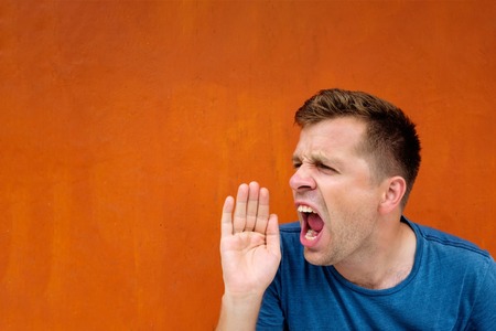 Young caucasian man yelling or shouting in anger on red backgroundの写真素材