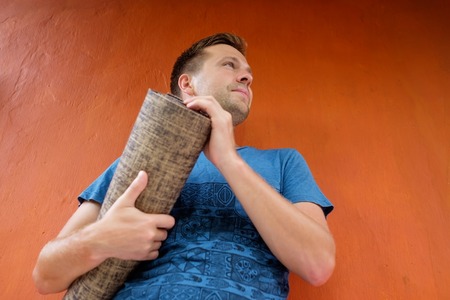 Caucasian man holding yoga mat in hands and standing near red background.の写真素材