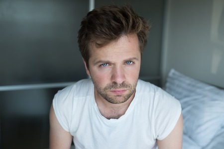 Serious man looking at camera sitting on bedの写真素材