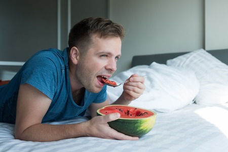 Caucasian man eating watermelon at homeの写真素材