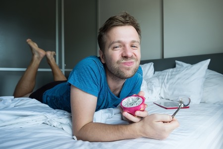 caucasian man eating dragon fruie with spoon in the bed.の写真素材