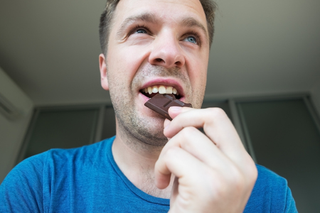 Young caucasian guy eating a chocolate aloneの写真素材