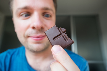 Young caucasian guy eating a chocolate aloneの写真素材