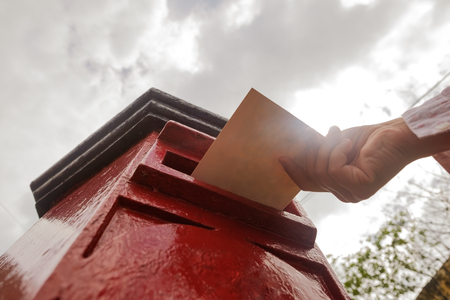 Closeup on a male hand putting a letter in a red letterbox. Concept of vintage type of communication.の写真素材