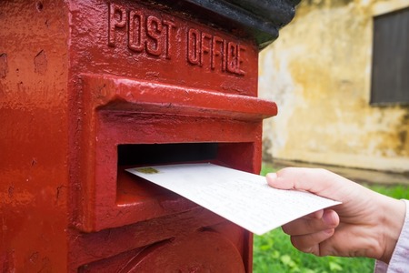 Closeup on a male hand putting a letter in a red letterbox. Concept of vintage type of communication.の写真素材