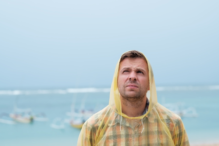 Caucasian man standing near sea on the beach wearing raincoat.の写真素材
