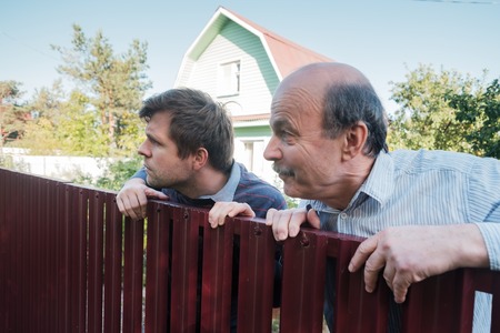 two caucasian men carefully watching over the fence.の写真素材