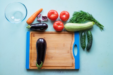 Layout of whole and sliced eggplants, cutting board and other fresh vegetables.の写真素材