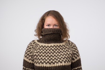 Woman in warm brown sweater hiding her face. Only eyes are seen. She wants to stay anonym.