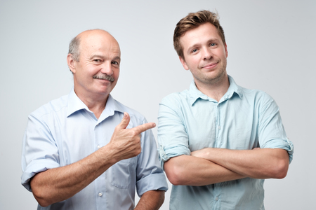 Senior father is proud of his mature son. He is pointing on him saying it is my boy.の写真素材