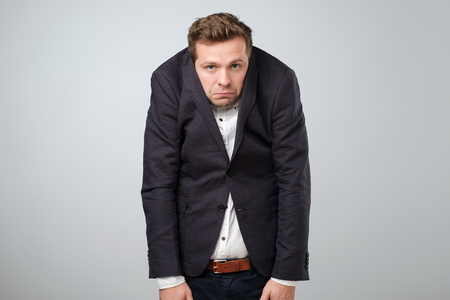 Caucasian young man in too big suit. He is offended and looking stressed. Looking silly in a suit of wrong sizeの写真素材