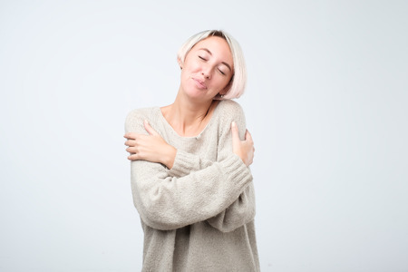 Closeup portrait, confident woman in warm sweater holding hugging herself, isolated white background. Positive emotion facial expression feeling, reaction, situation, attitude. Love yourself conceptの写真素材