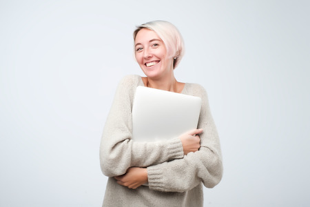 Cheerful young woman with dyed short hair standing, holding laptop computer, making presentation. Hipster female smiling, surfing, browsing, blogging.の写真素材