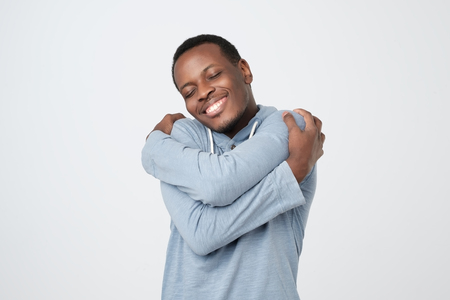 Funny playful african guy cuddling himself and smiling from pleasureの写真素材