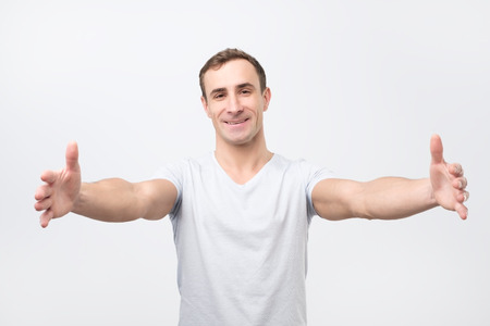 Handsome guy pulling hands towards camera and smiling friendly at camera wanting hugの写真素材