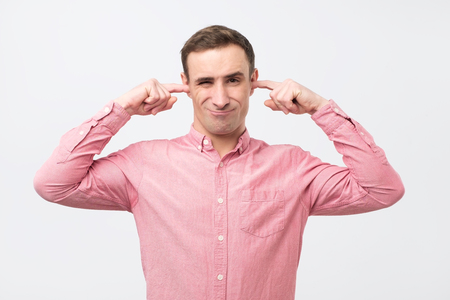 Mature man with annoyance closing ears with fingers not wanting to hear something. Stressed young italian man plugging his earsの写真素材