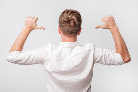 Caucasian young man turning back to the camera and pointing at his hairstyle.の写真素材