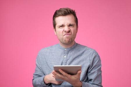 angry european man with a tablet on a pink backgroundの写真素材