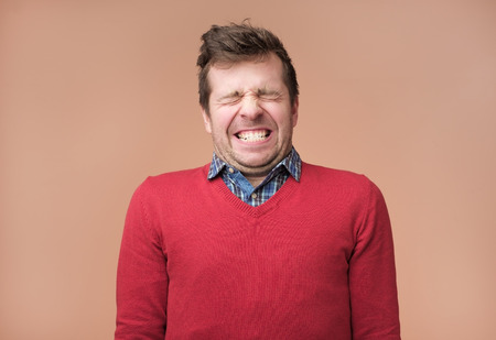 Positive middle aged guy in red sweater grins at camera, shows white teeth, closes eyeswaiting for giftの写真素材