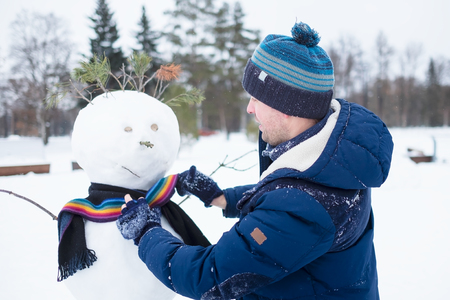 Young european man in warm clothes making snowman from snow outdoor. Having fun like a child at winter vacation.の写真素材