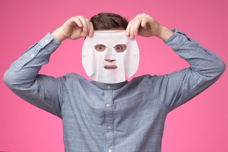 Young european man in facial mask on pink background. Grooming himself, taking care about his skinの写真素材