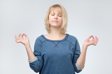 Young calm yogi woman wearing blue sweater practicing yoga, meditating with closed eyes, relaxing and working out.の写真素材