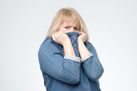 Blonde girl in blue sweater pulling her trendy sweater over head.