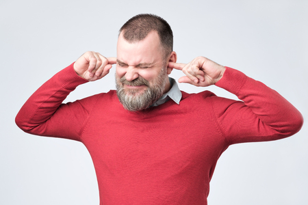 Senior man, covering closed ears annoyed by loud noise not wanting to hear storyの写真素材