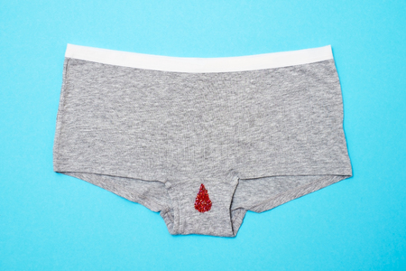 Red drop from beads on pants on blue background. Menstruation period
