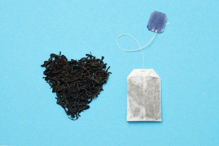 Tea bag and black leaves on blue background. What kind of tea is betterの写真素材