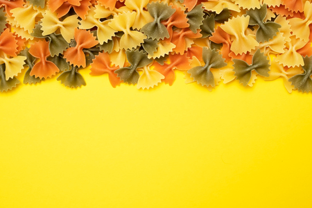 Raw farfalle pasta stack top view isolated on yellow background