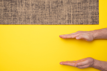 New yoga mat on a colored yellow background. Man hand show small size.の写真素材
